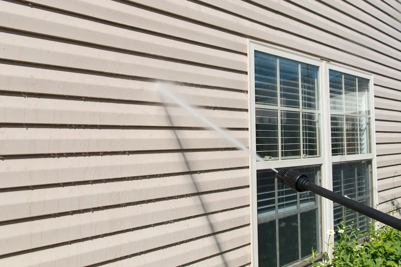 A person is using a high pressure washer to clean the side of a house.