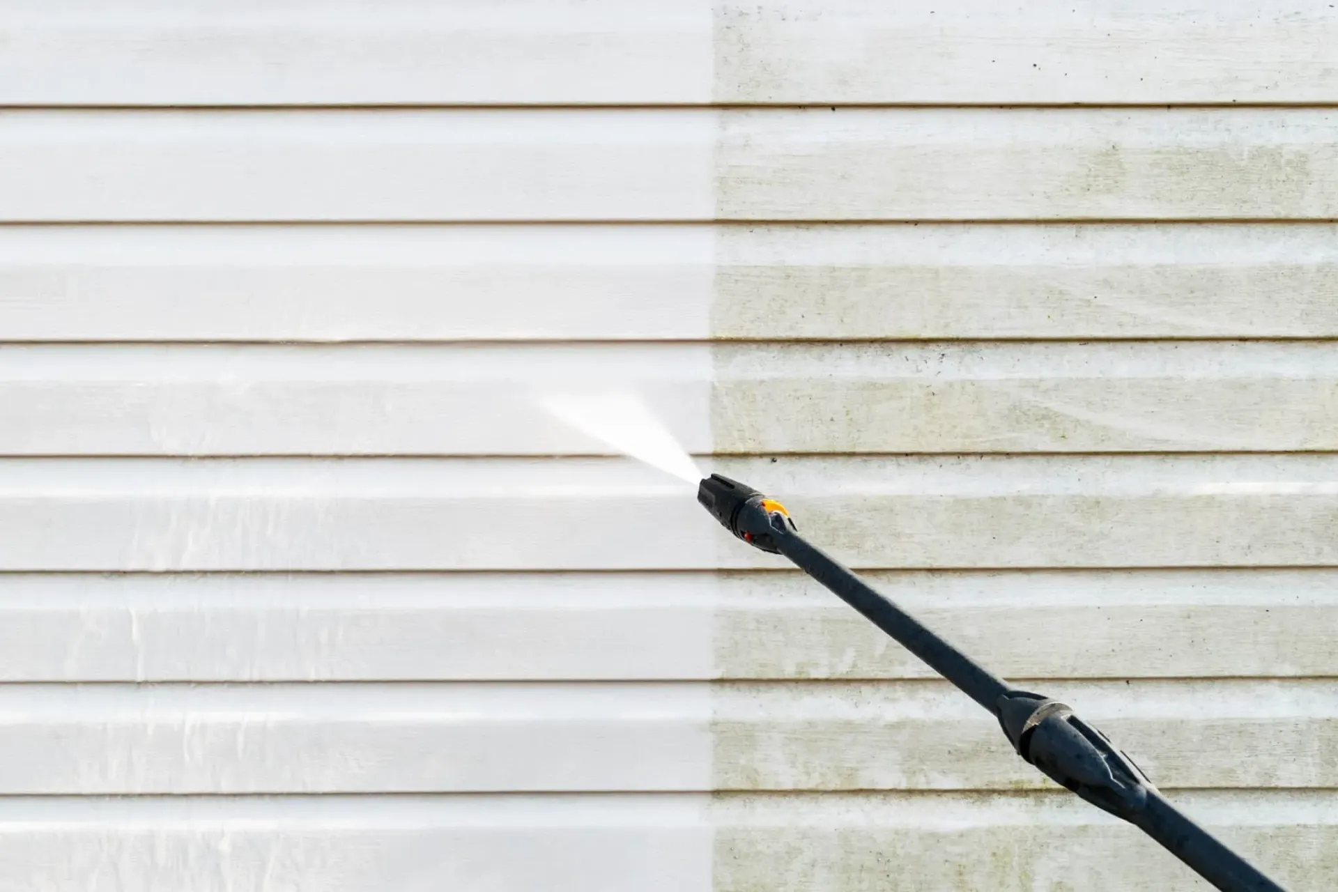 A person is cleaning the side of a house with a high pressure washer.