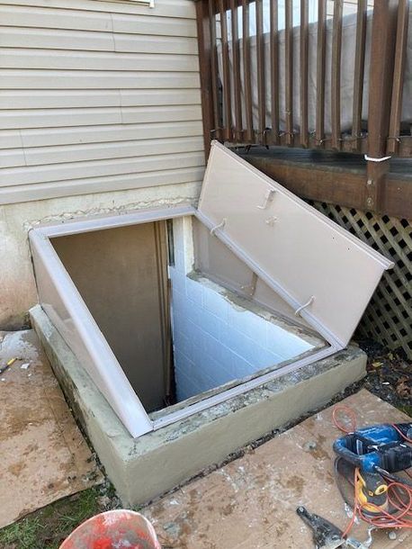 A basement window with the lid open is being built next to a house.