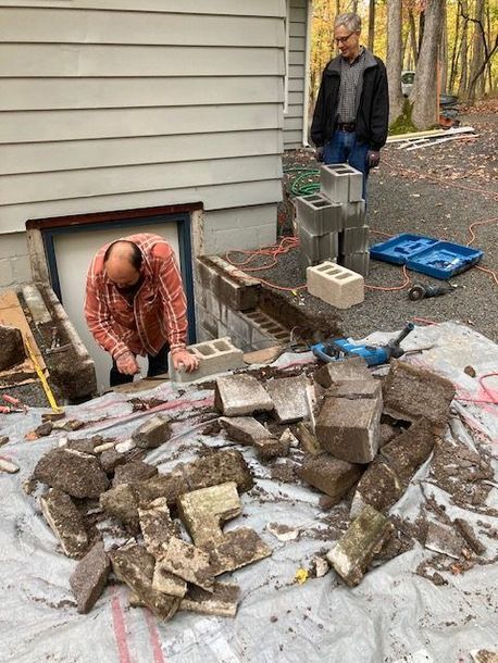 Two men are working on a brick wall in front of a house.