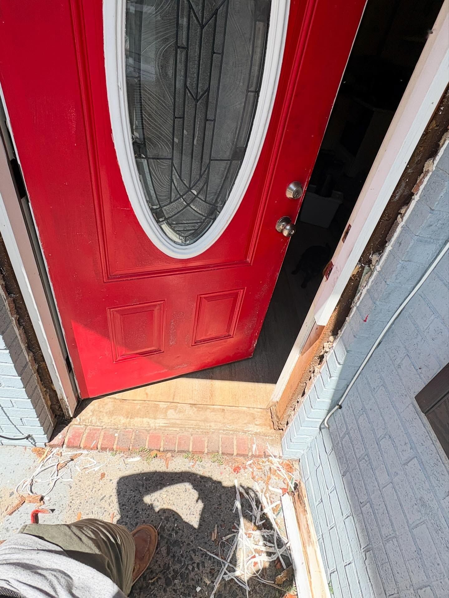 Red front door with oval window, viewed from outside on a sunny porch step.