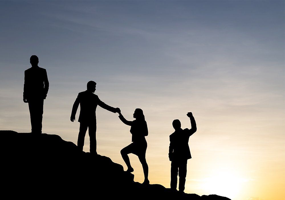 Silhouette of businessman helping each other hike up a mountain at sunrise