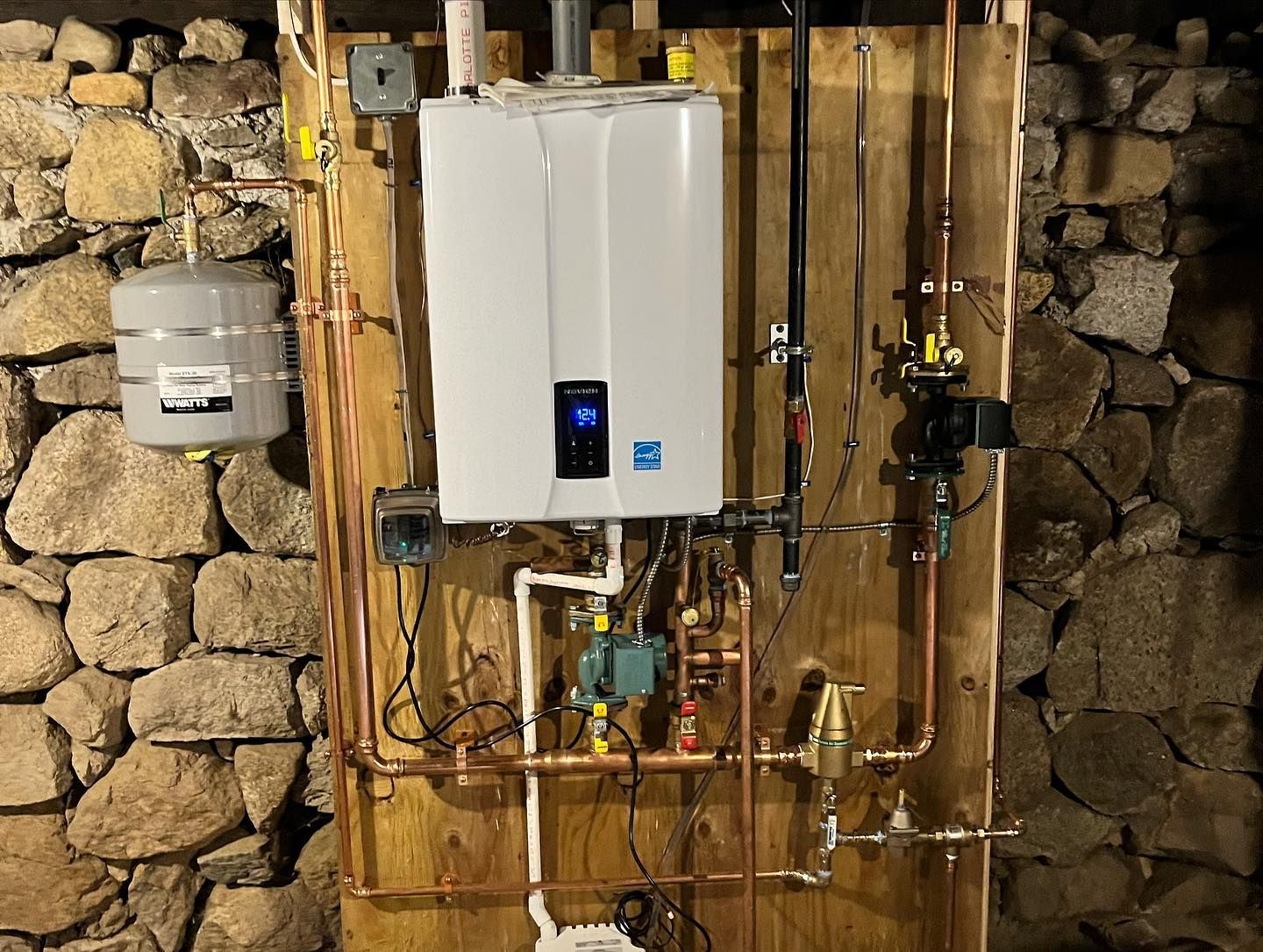 A white water heater is mounted to a wall next to copper pipes.