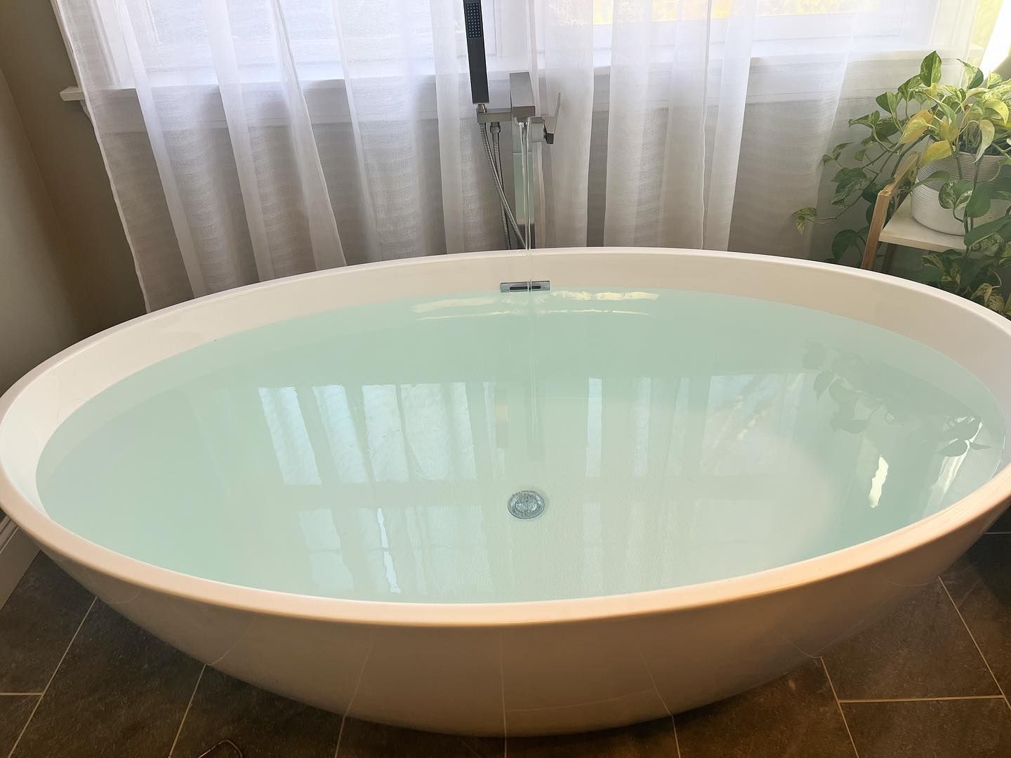 A bathtub filled with blue water in a bathroom next to a window.