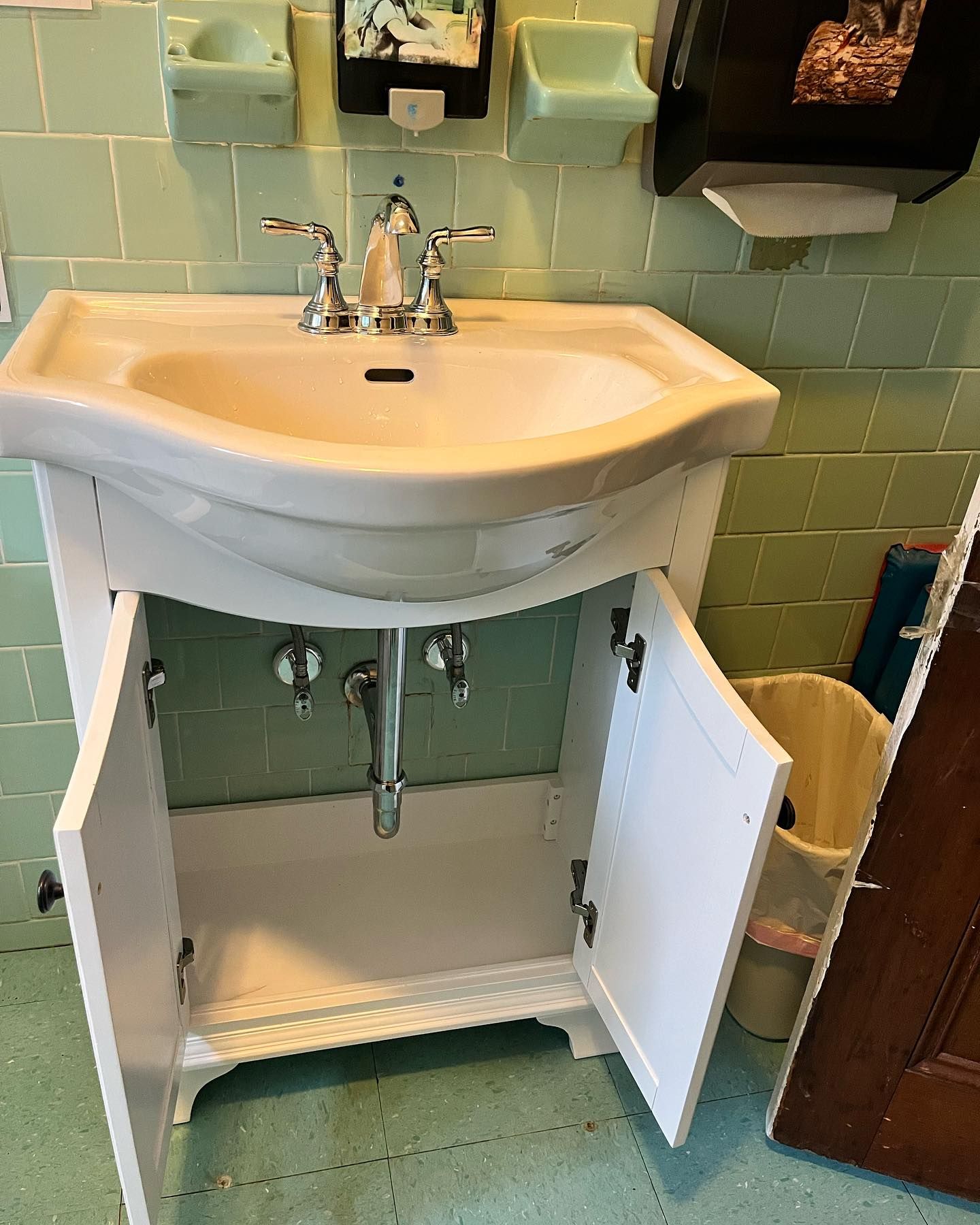 A bathroom sink with its cabinet open and a trash can next to it.