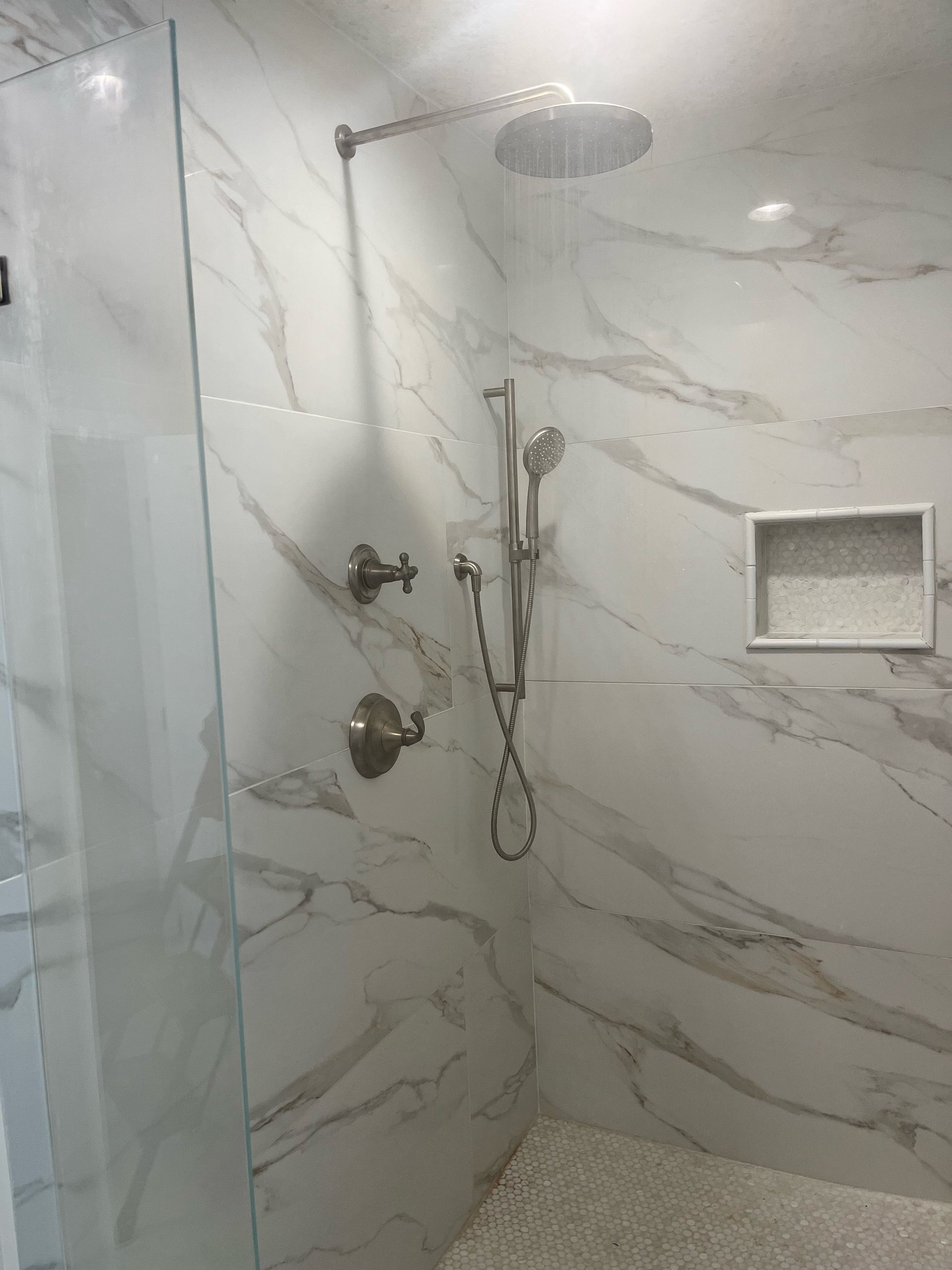 A bathroom with marble tiles and a walk in shower with a shower head.