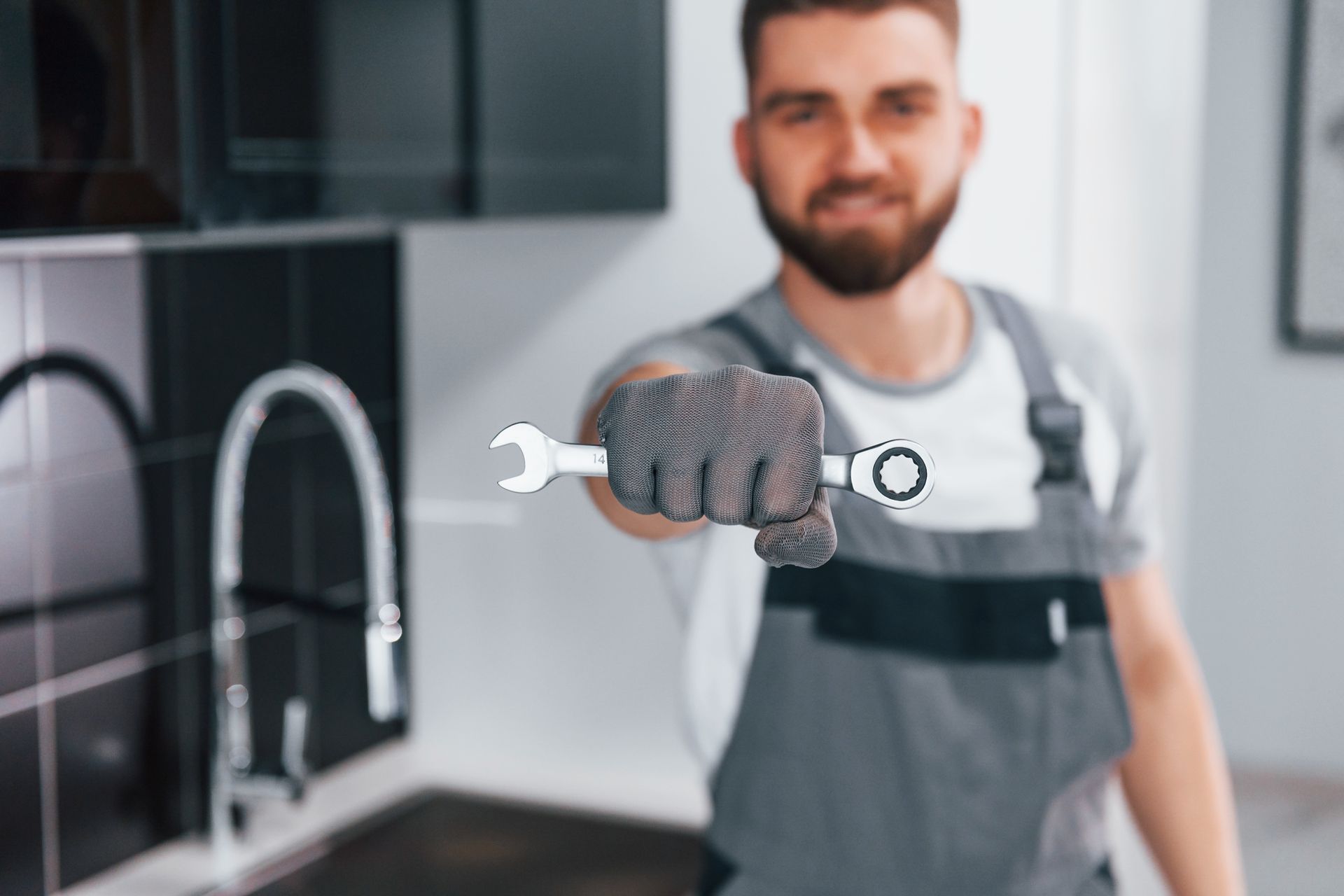 A man is holding a wrench in his hand in a kitchen.