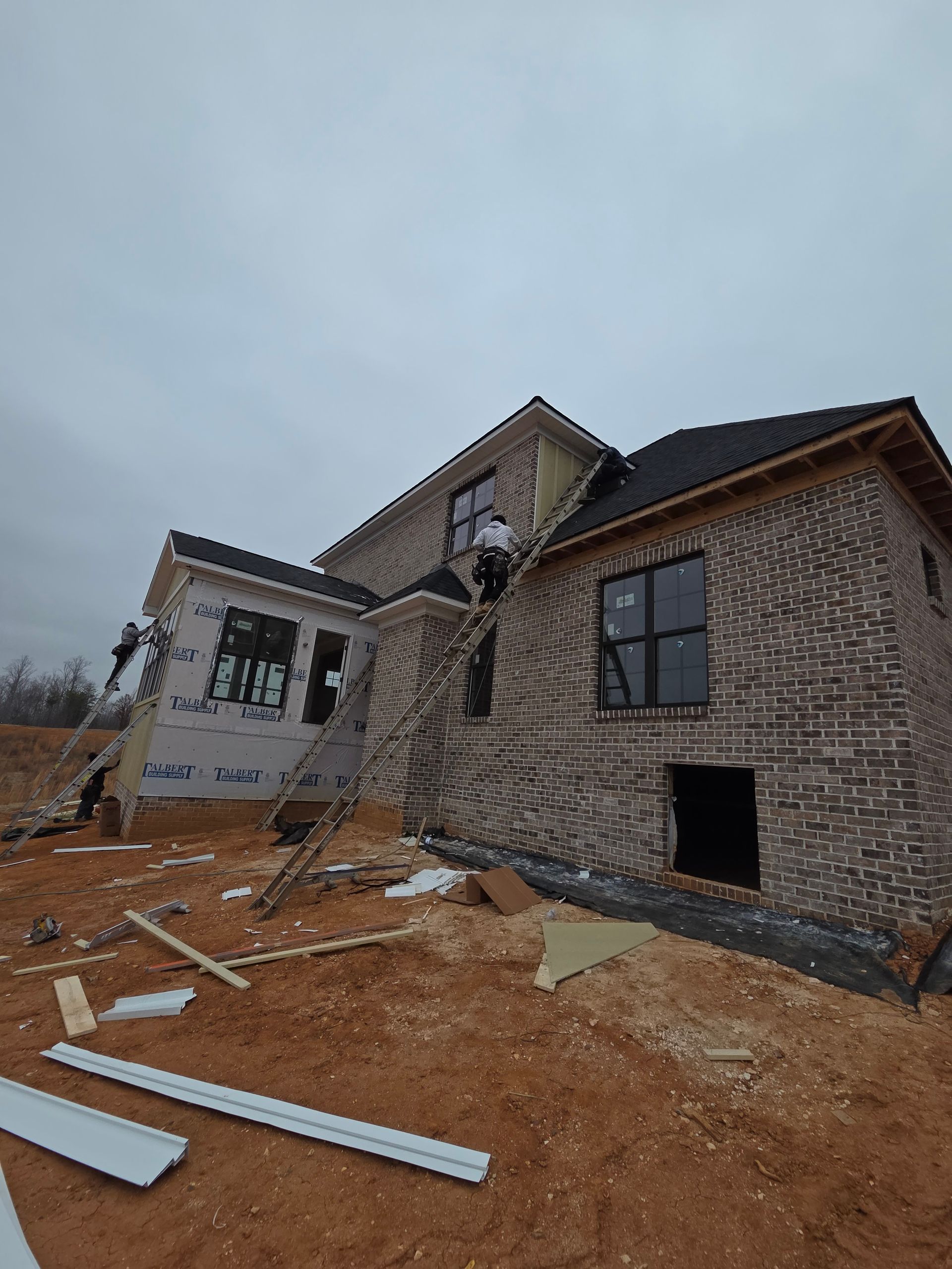 Man in overalls installing a window frame in a room with gray walls.