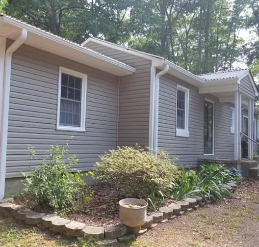 Tan house with white trim, small garden, and trees.
