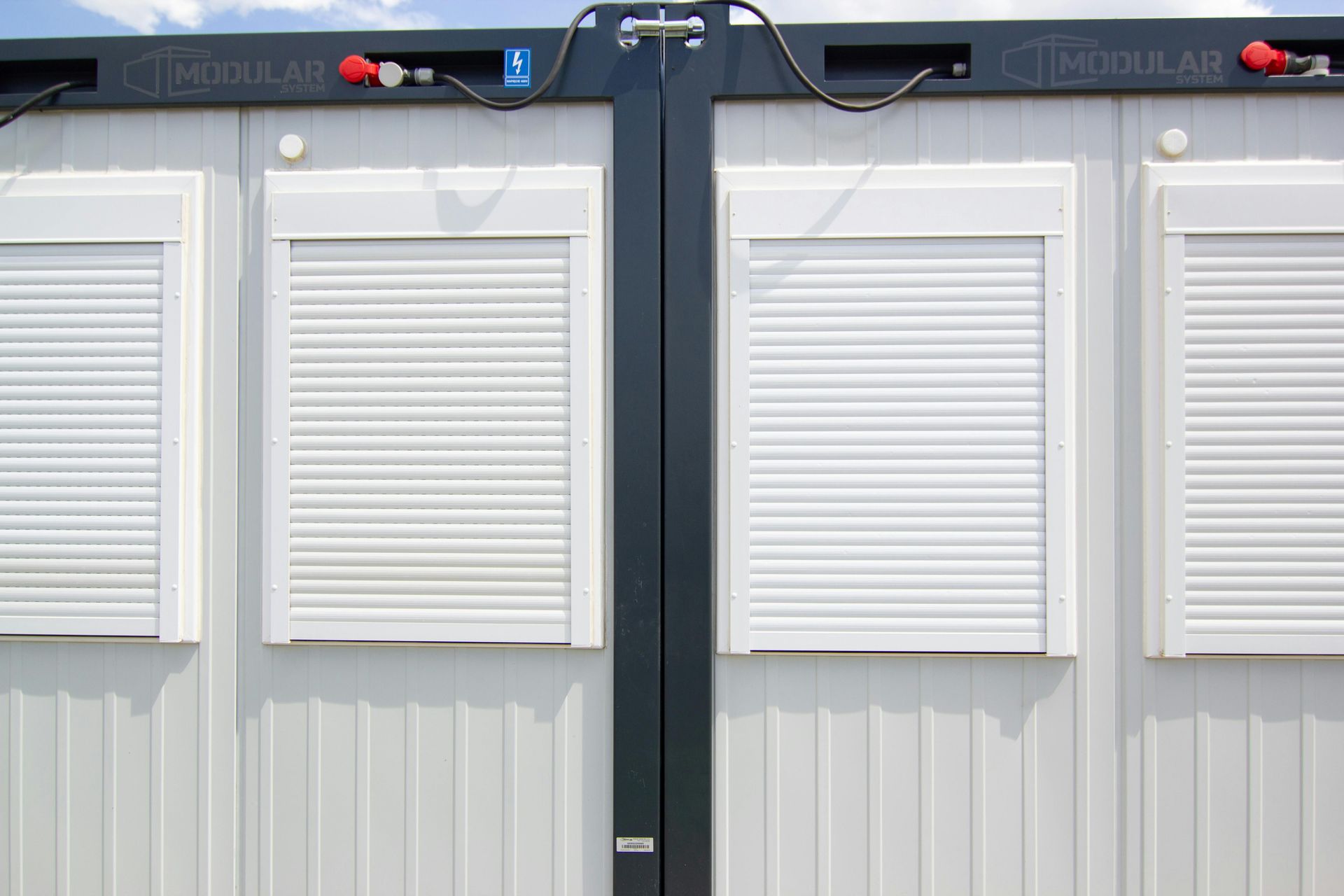 White building with four windows, each covered by a closed, white rolling shutter.