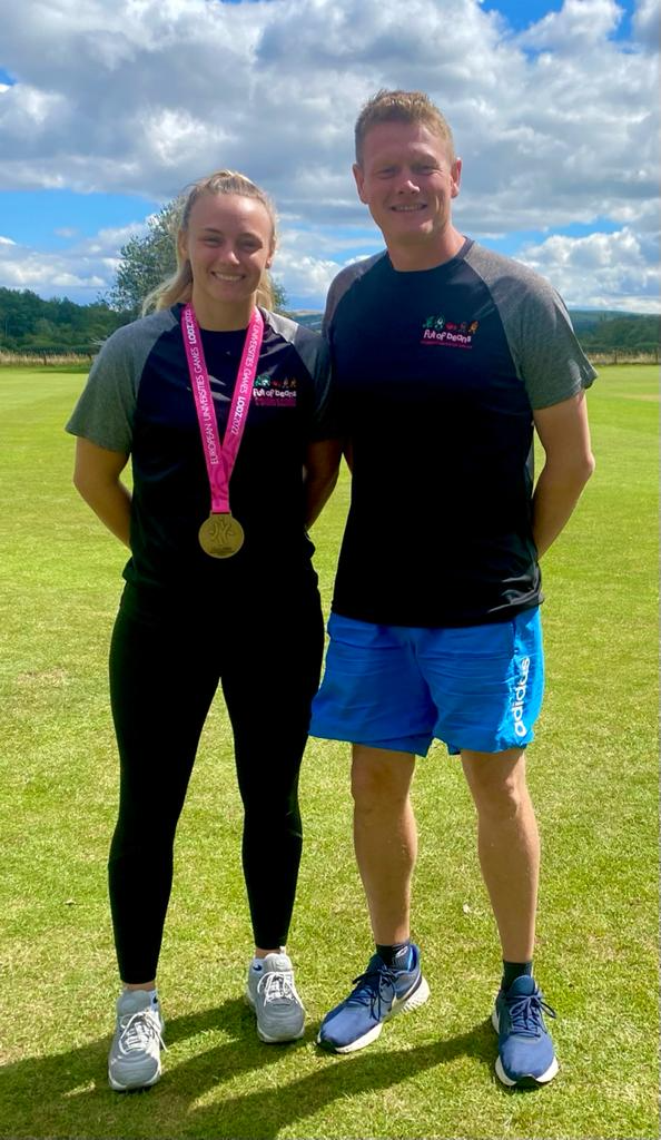 A man and a woman are standing next to each other in a field . the woman is wearing a medal.