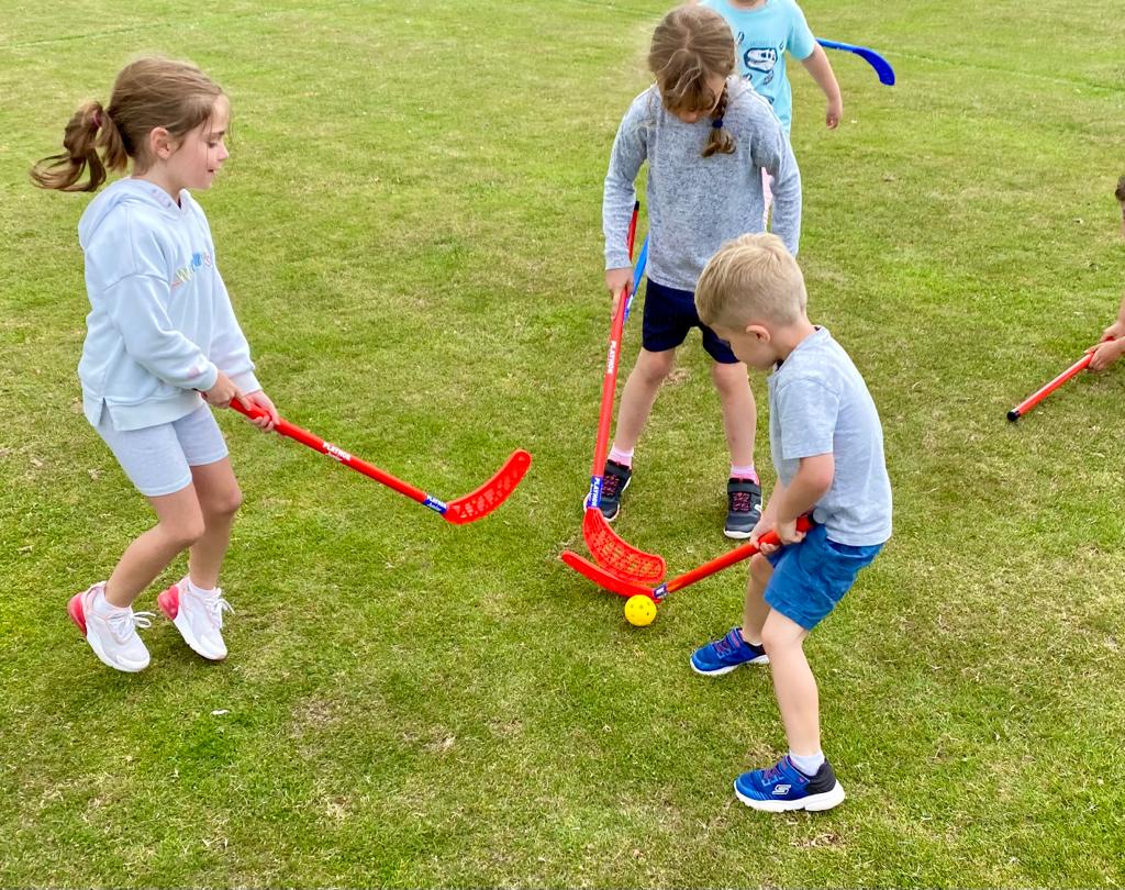 A group of children are playing a game of lacrosse on a lush green field.
