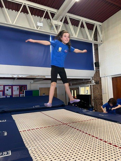 A young girl is jumping on a trampoline in a gym.