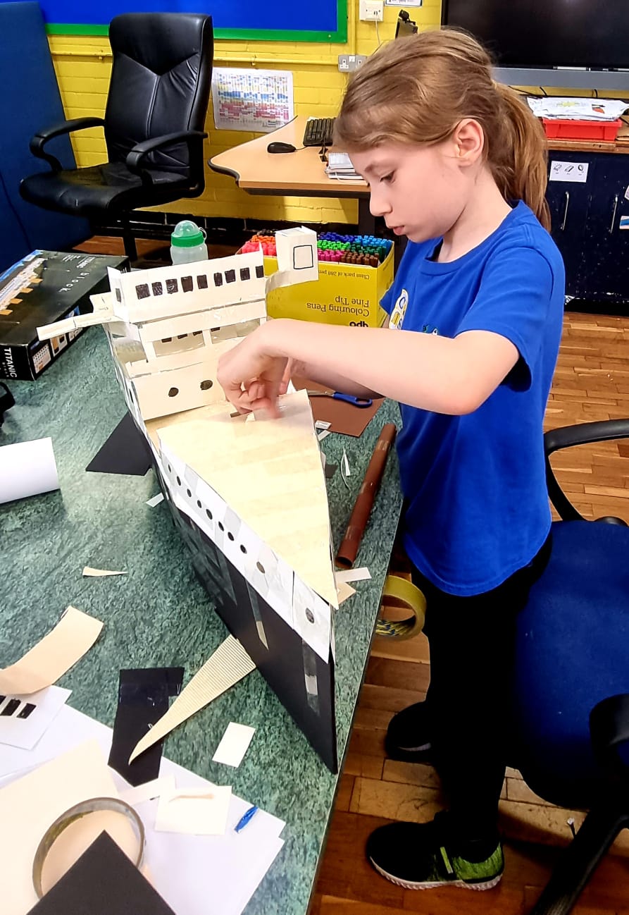 A young girl is working on a model of the titanic ship.