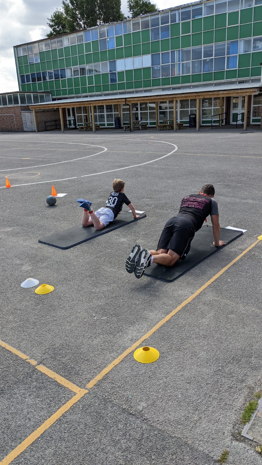 Two men are doing push ups on yoga mats in a parking lot.