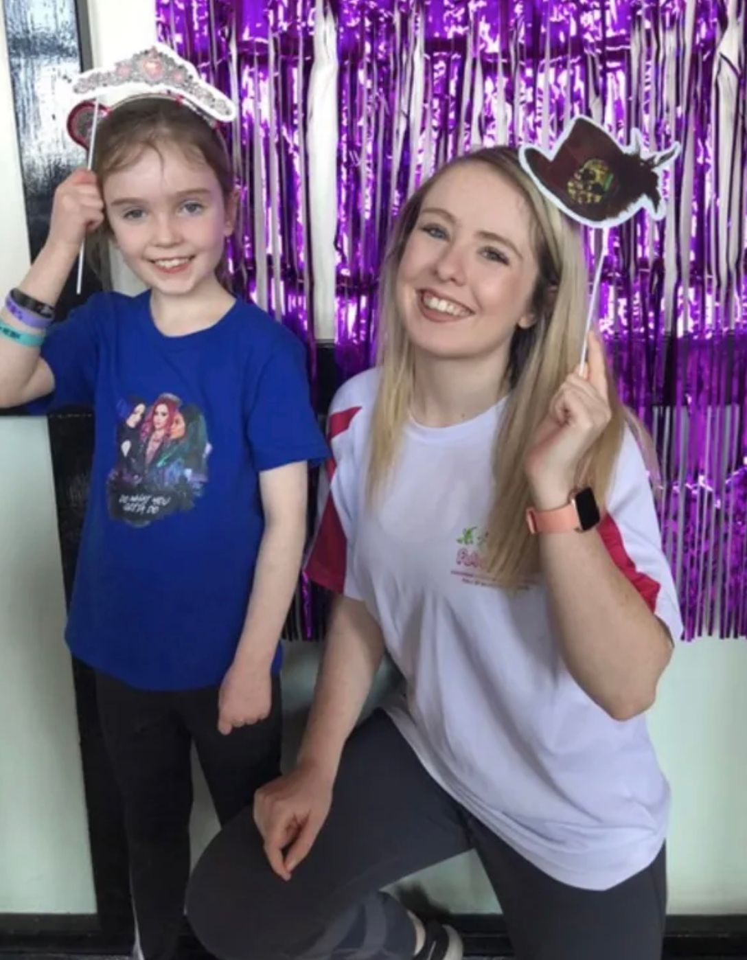 A woman and a little girl are posing for a picture in front of purple tinsel.
