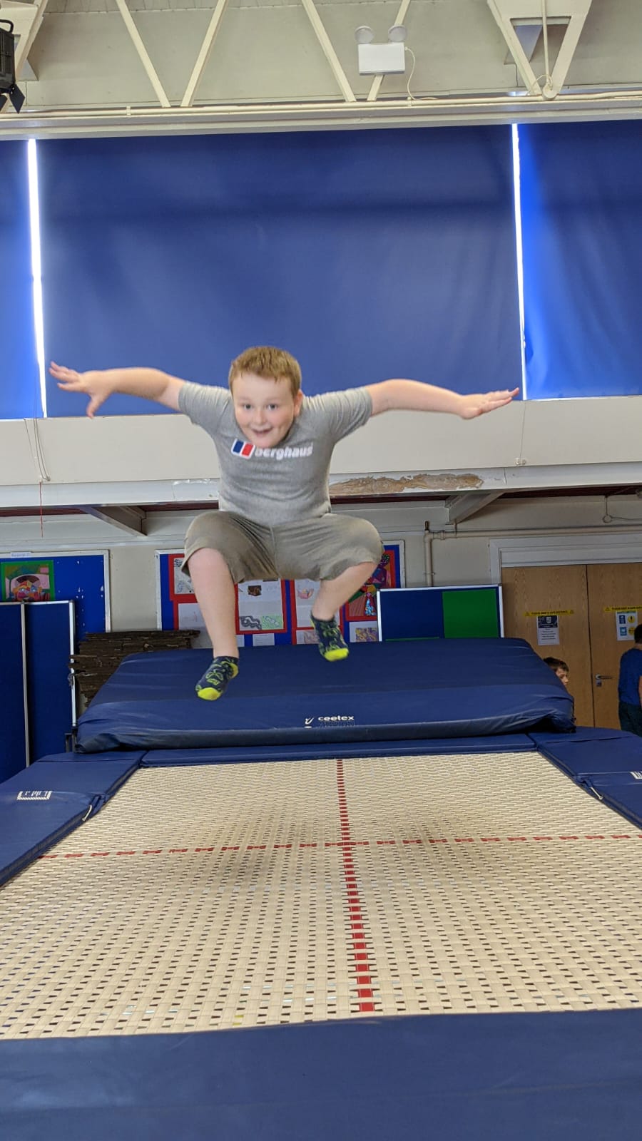 A young boy is jumping on a trampoline in a gym.