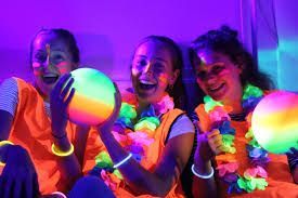 Three girls are sitting next to each other in a dark room holding glow in the dark balloons.