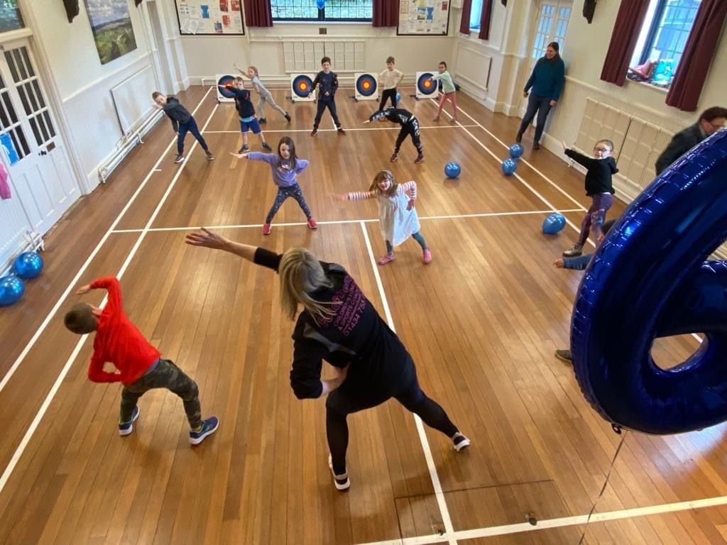 A group of children are standing on a wooden floor in a gym.
