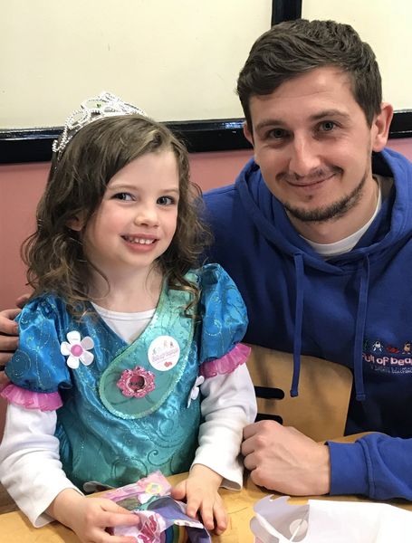 A man and a little girl are posing for a picture . the little girl is wearing a tiara.