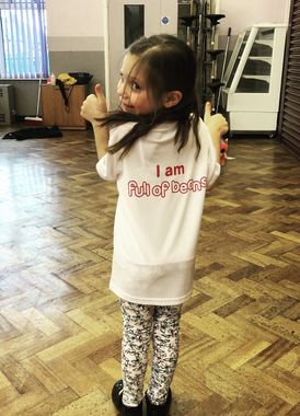 A little girl wearing a white shirt that says i am full of best is giving a thumbs up