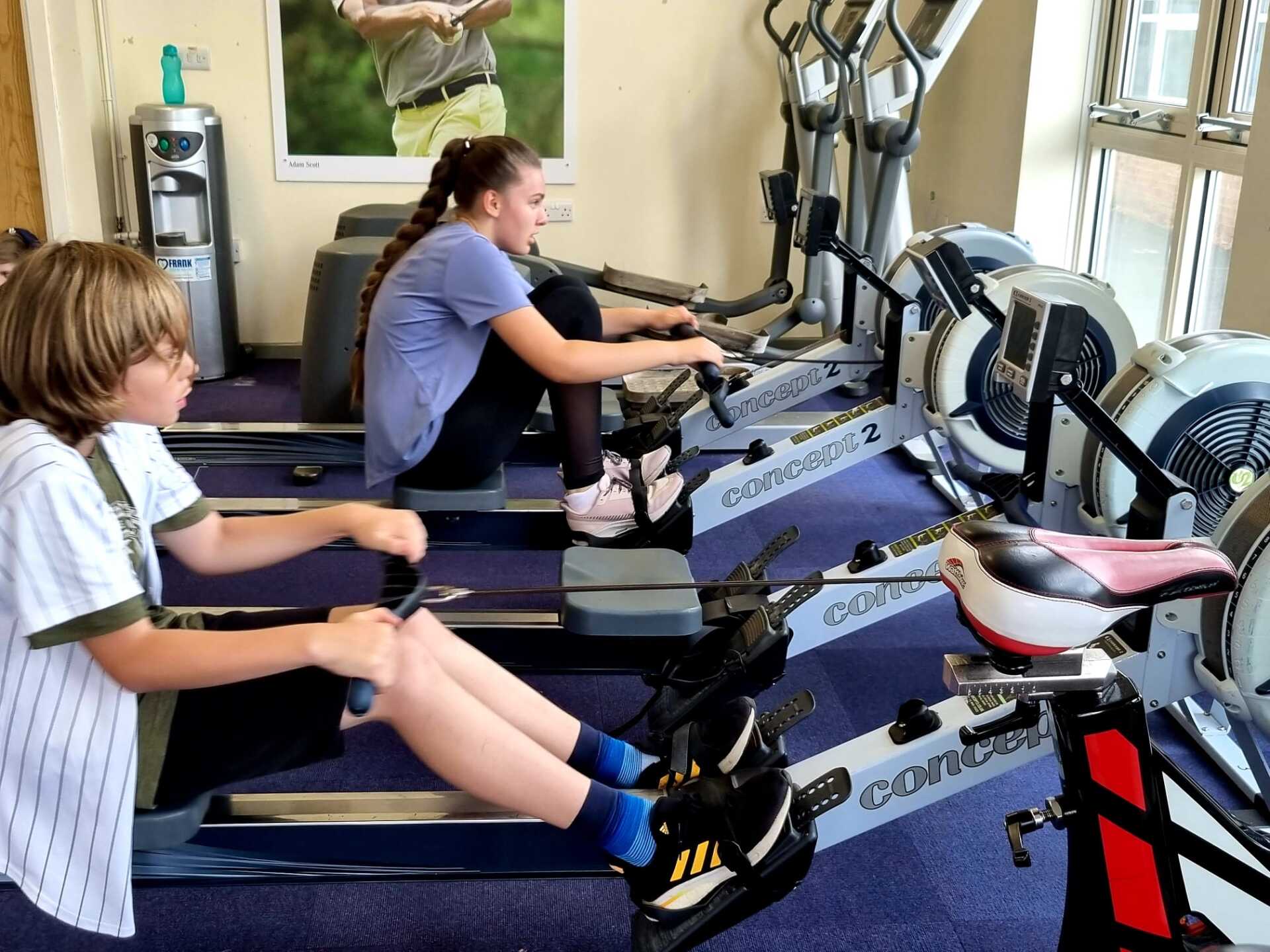 A boy and a girl are rowing in a gym.