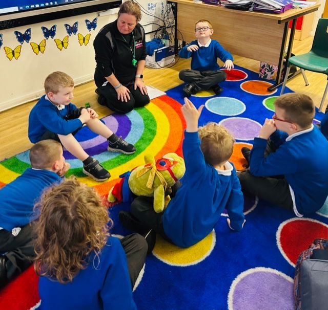 A group of children are sitting in a circle on a rainbow rug