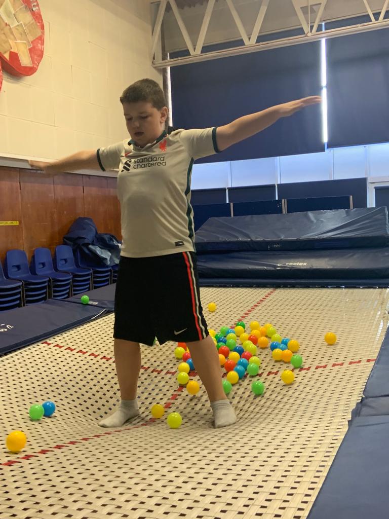 A young boy is standing on a trampoline surrounded by colorful balls.