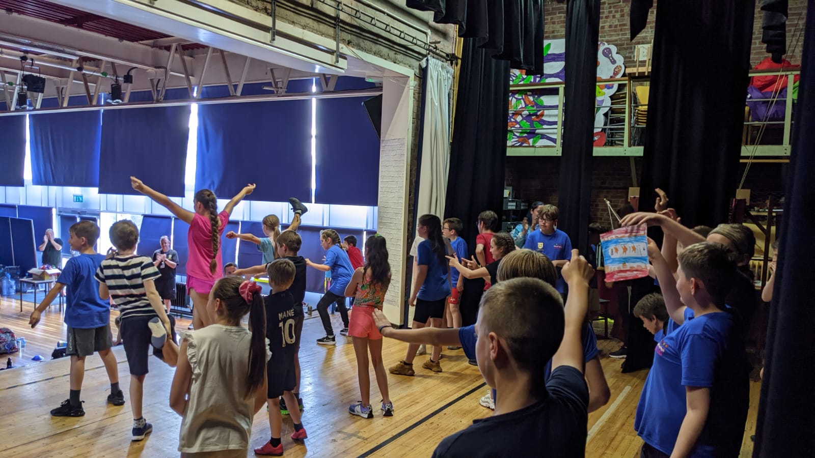 A group of children are dancing on a stage in a gym.