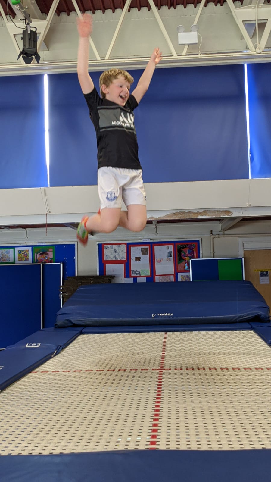 A young boy is jumping on a trampoline in a gym.