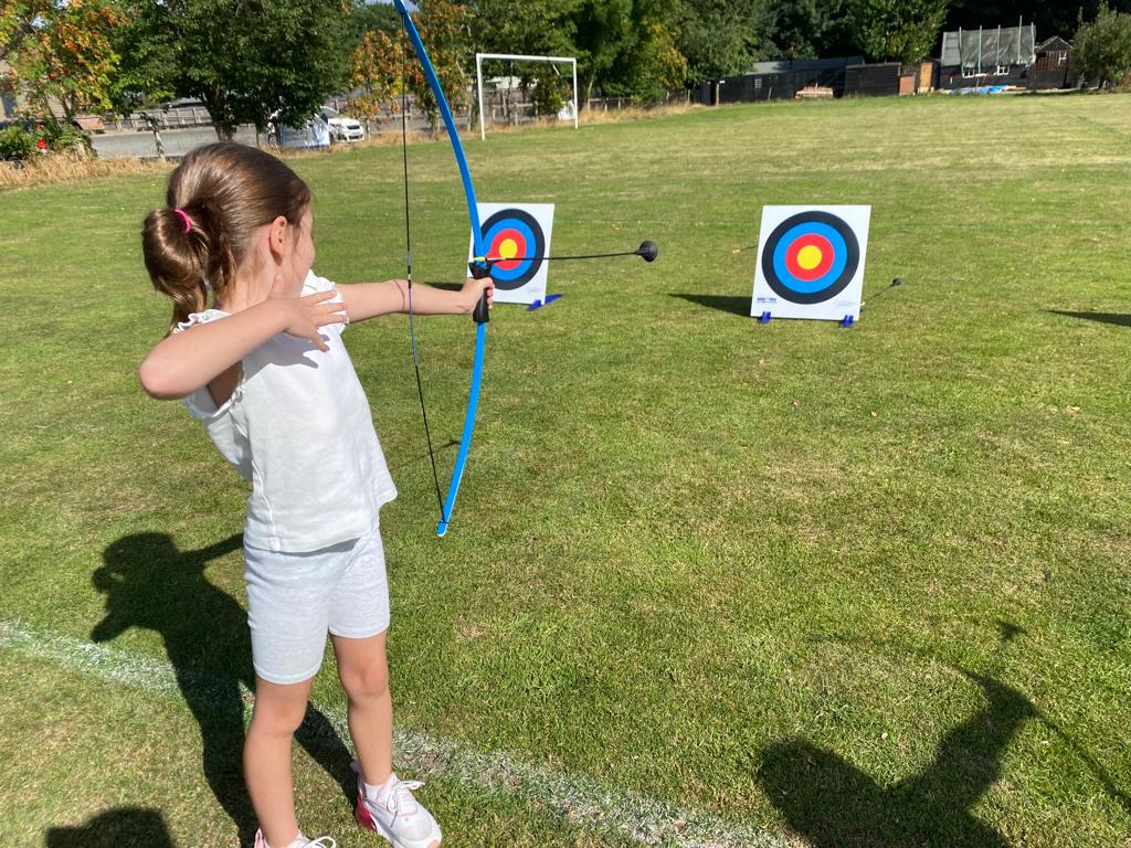 A little girl is practicing archery in a field.
