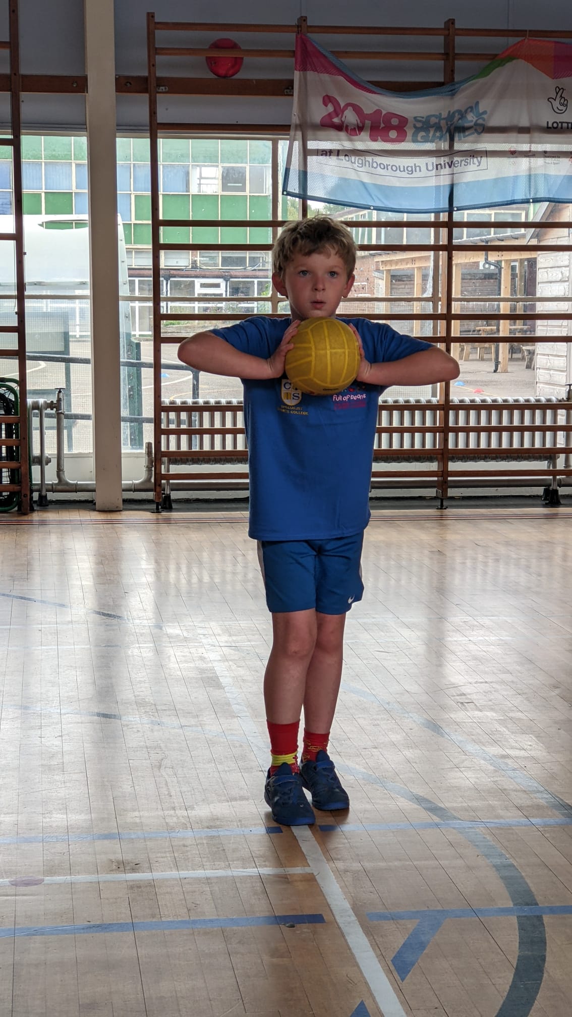 A young boy is standing on a basketball court holding a yellow ball.