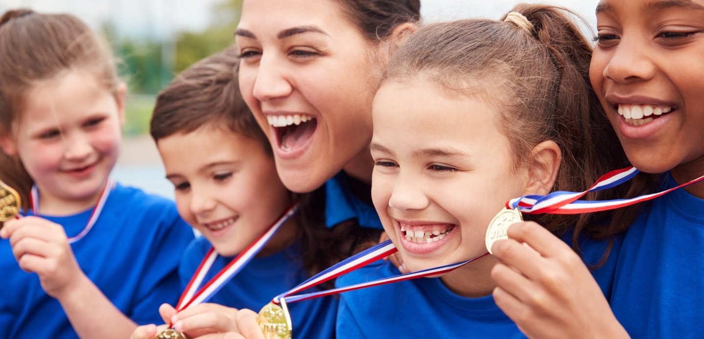 A group of children are holding medals around their necks and smiling.