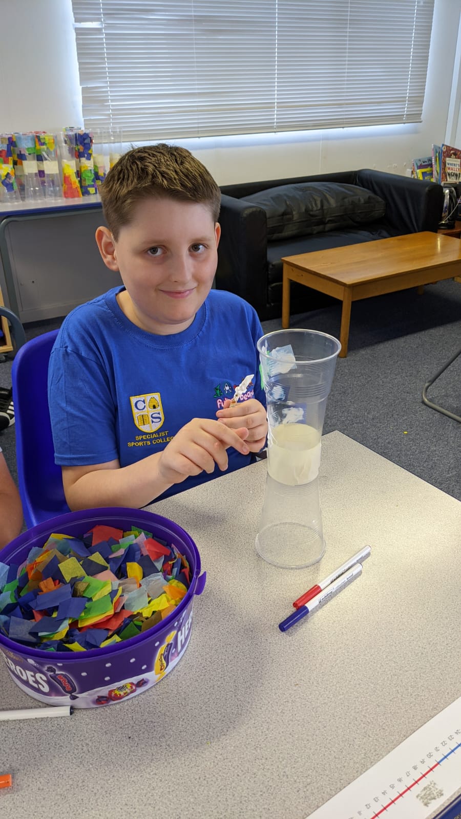 A young boy is sitting at a table holding a glass of liquid.