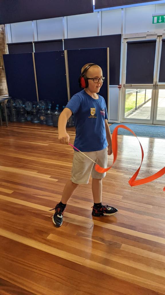 A young boy wearing headphones is holding an orange ribbon on a wooden floor.