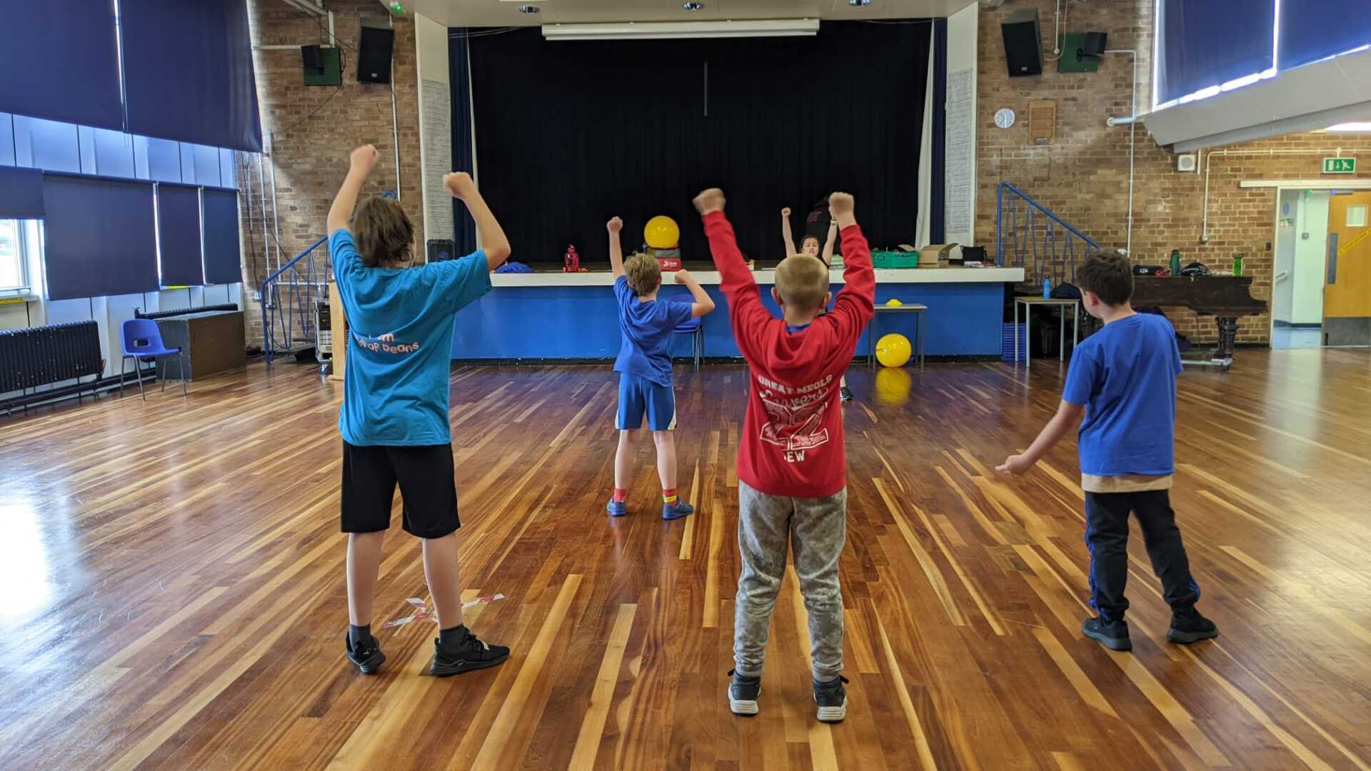 A group of children are standing in a room with their arms in the air.