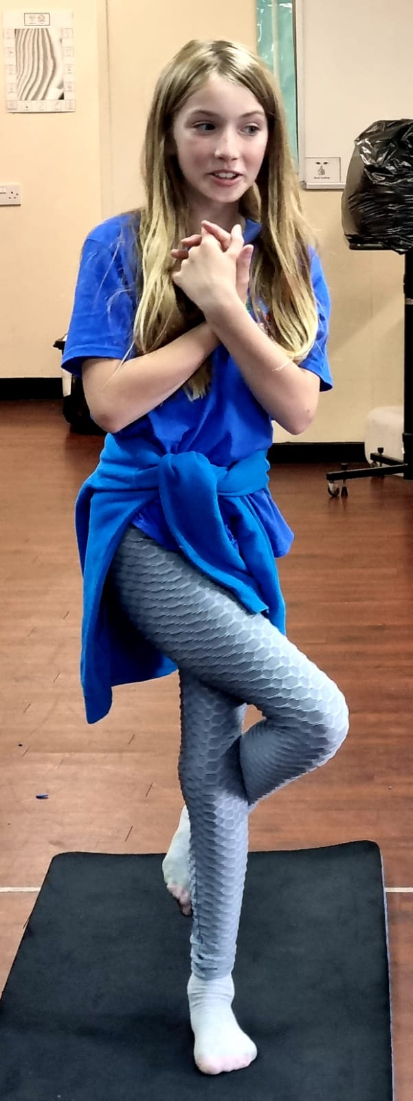 A young girl is standing on one leg on a yoga mat.