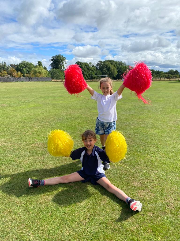 Two young girls are sitting on the grass holding pom poms.