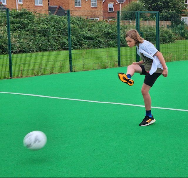 A young girl is kicking a soccer ball on a green field