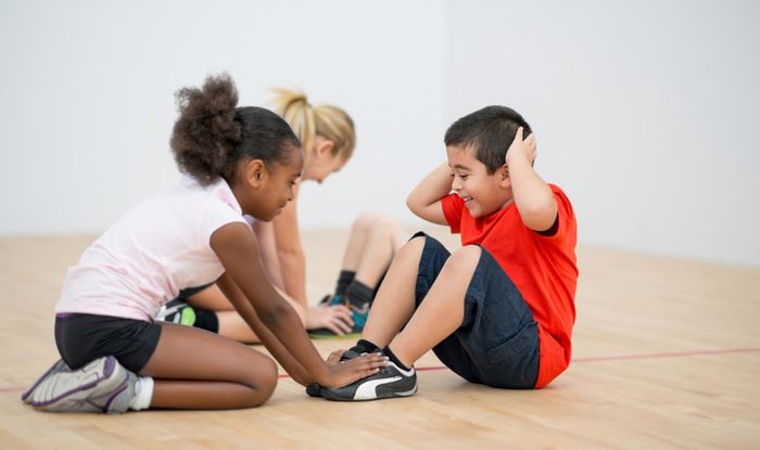 A group of children are sitting on the floor doing sit ups.