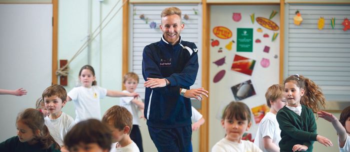 A man is dancing with a group of children in a classroom.