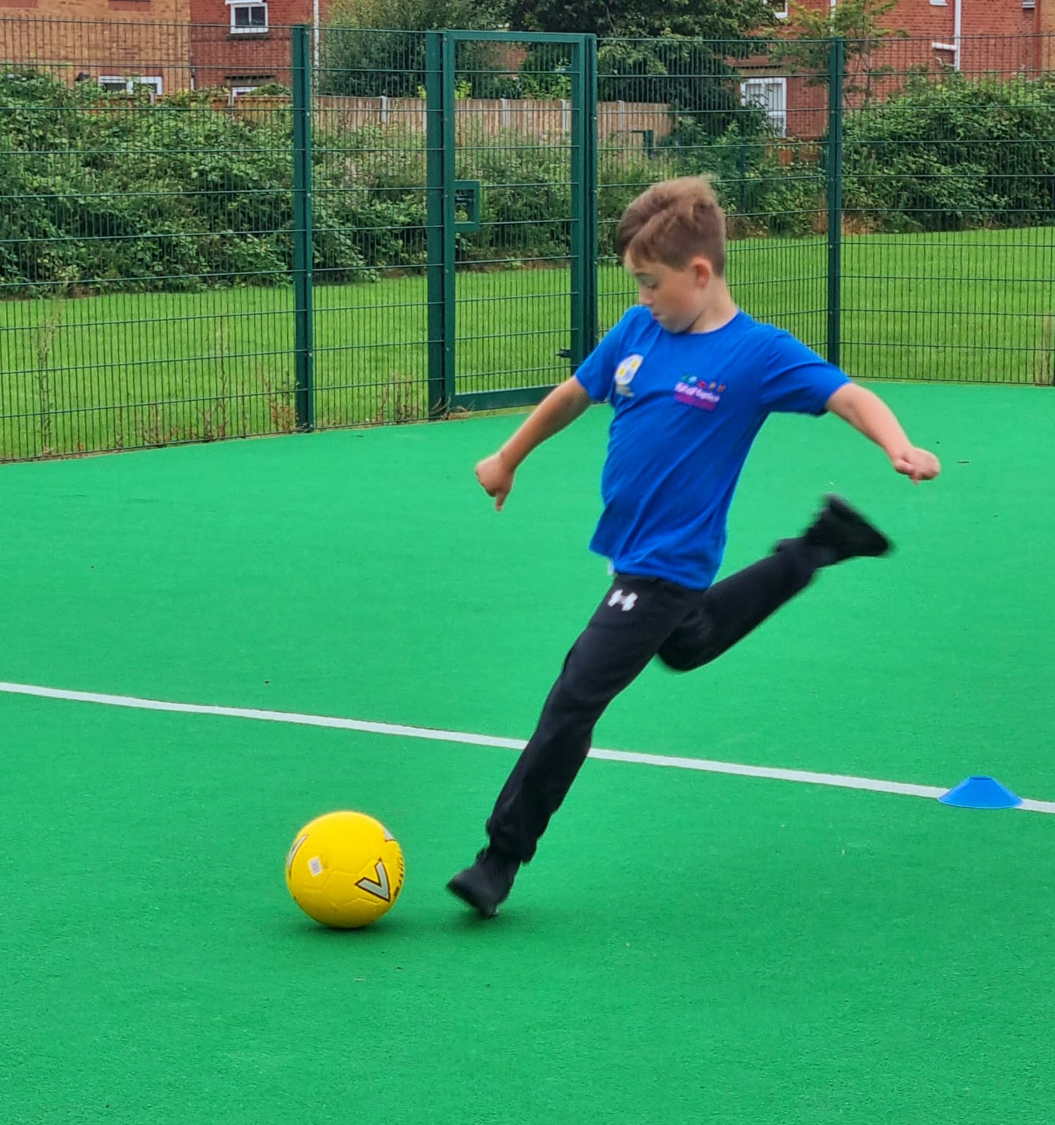 A young boy is kicking a soccer ball on a green field.