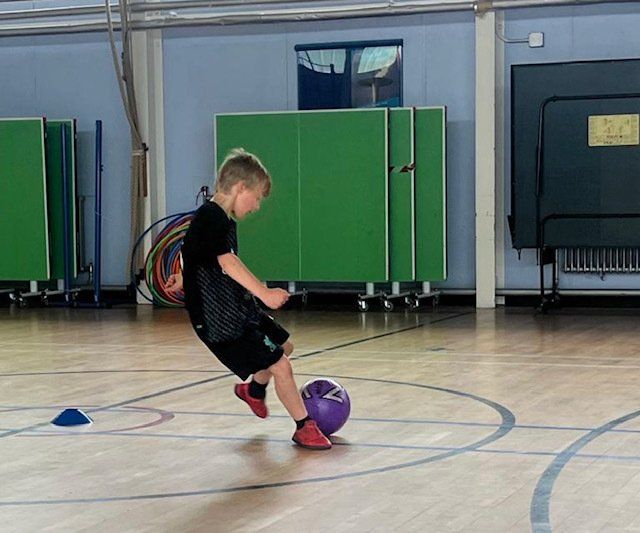 A young boy is kicking a soccer ball in a gym.