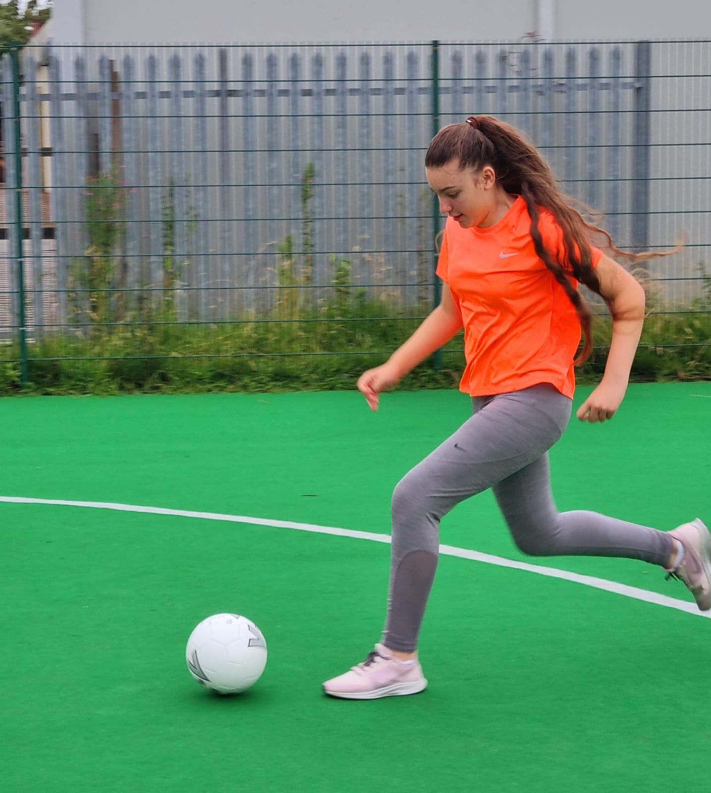 A woman is kicking a soccer ball on a green field.