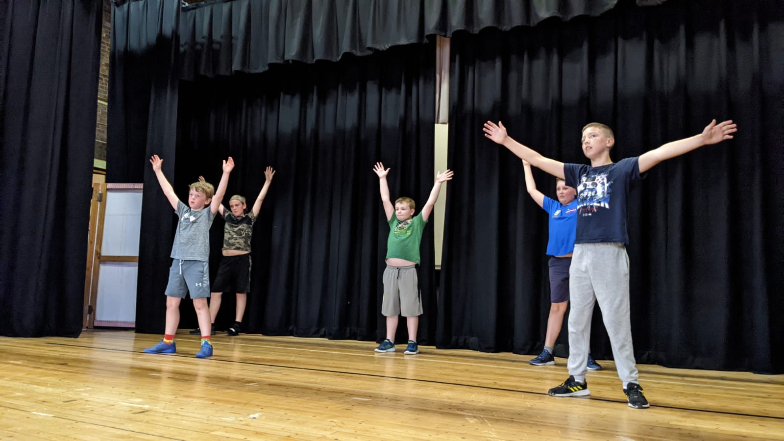 A group of young boys are standing on a stage with their arms outstretched.