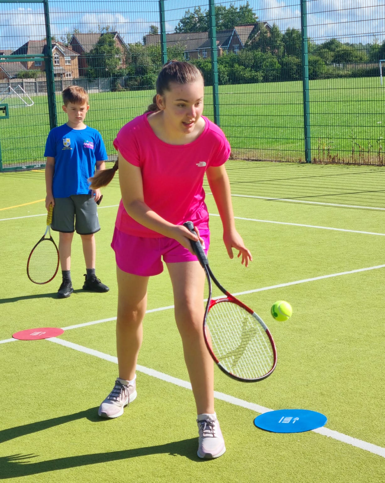 A girl in a pink shirt is playing tennis on a court