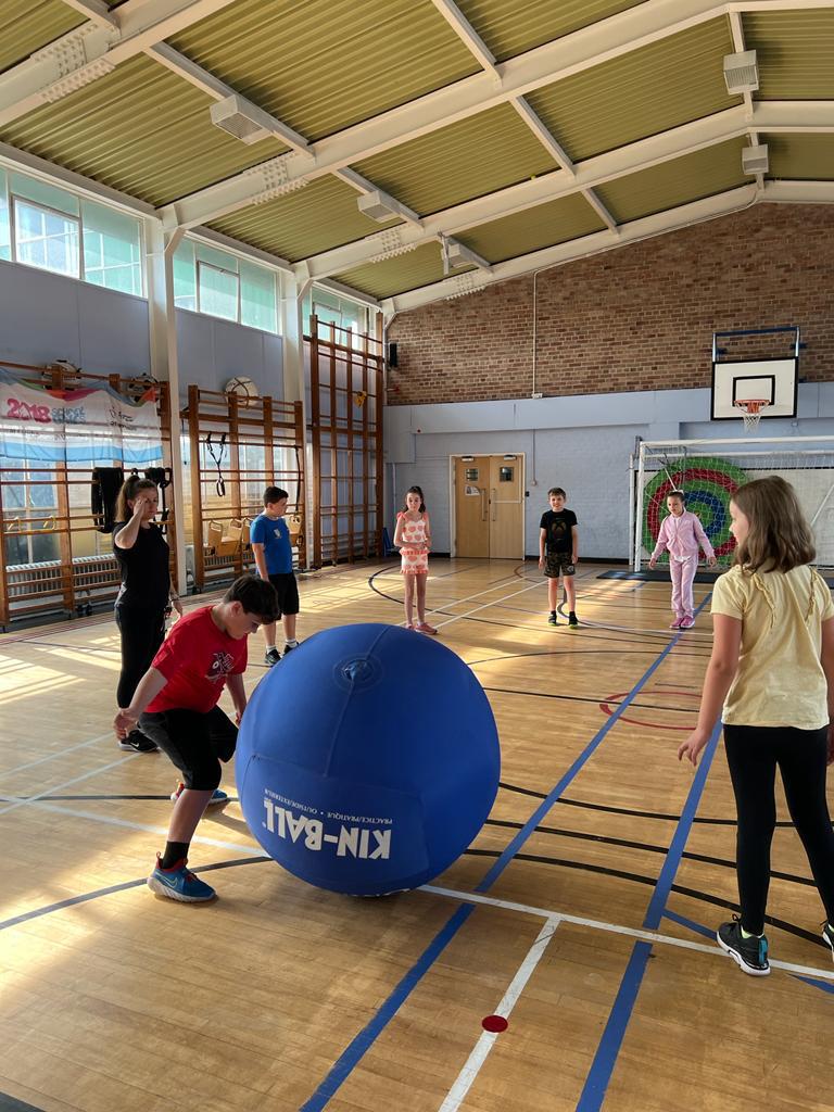 A group of children are playing with a large blue ball in a gym.