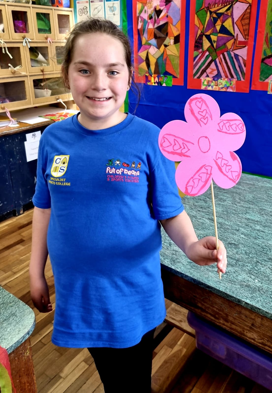 A girl in a blue shirt is holding a pink flower on a stick