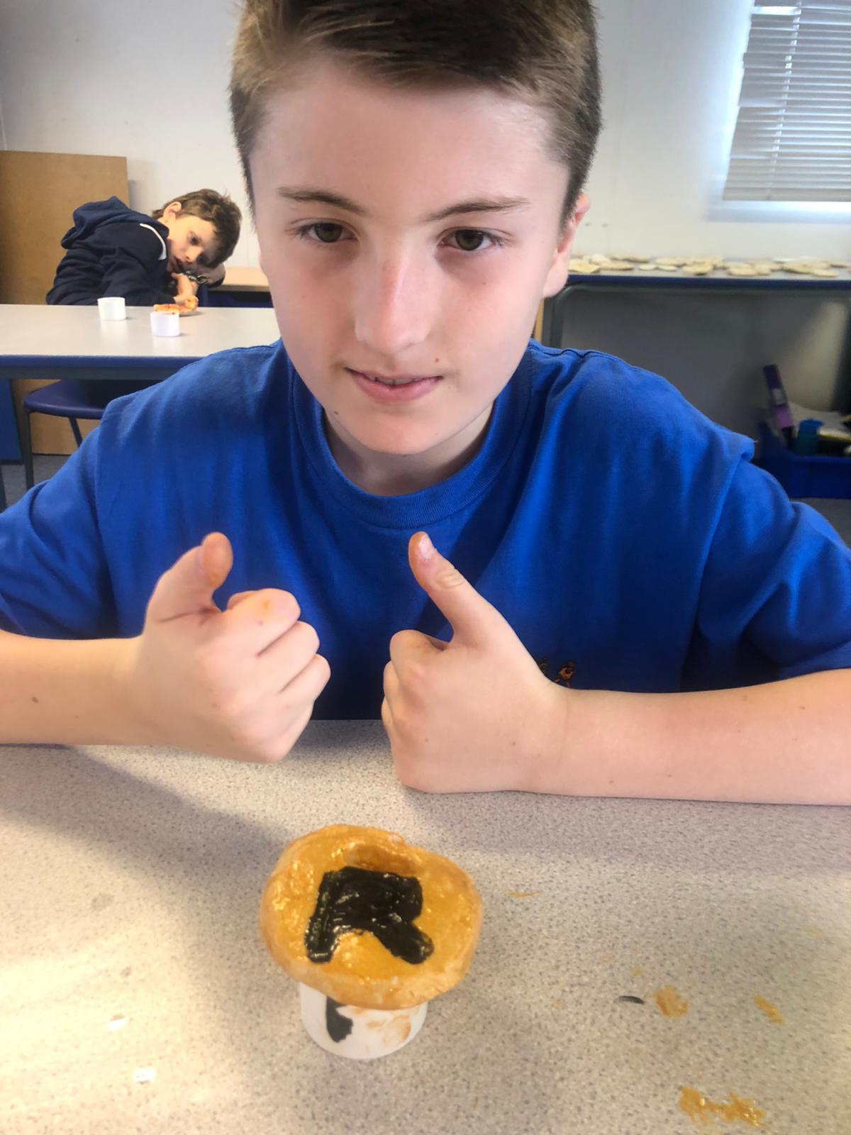 A boy in a blue shirt is giving a thumbs up next to a cup of food