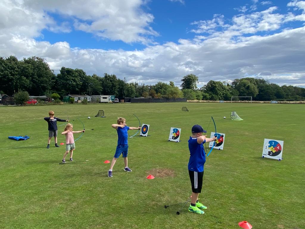 A group of children are playing archery in a field.